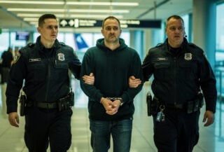 Federal agents escorting detainee through Atlanta airport terminal, fluorescent lighting