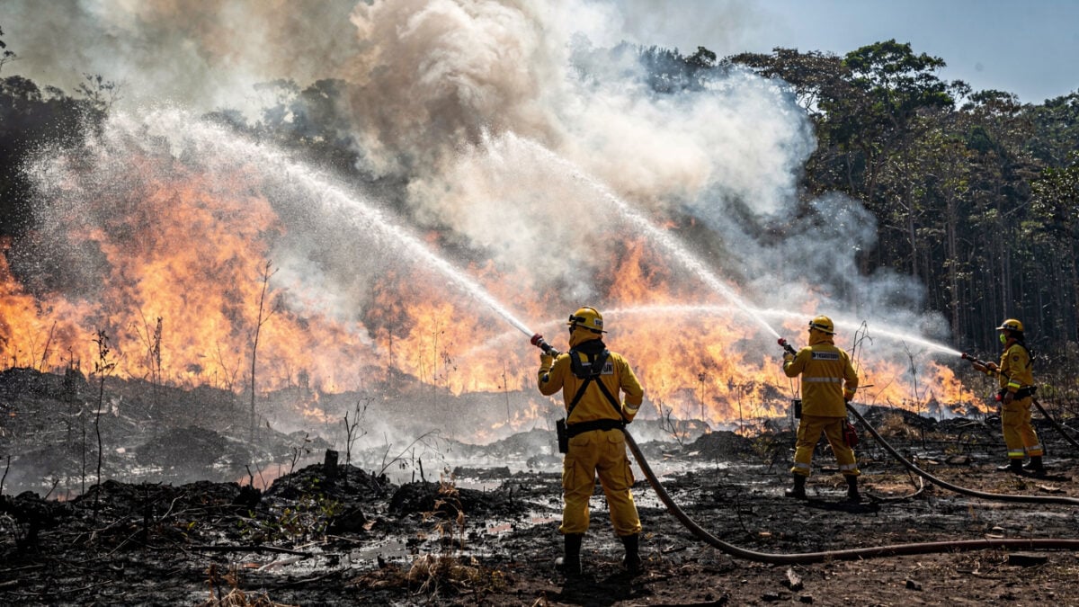 Firefighters spraying water at burning peatland forest in Kalimantan, thick smoke and flames visible