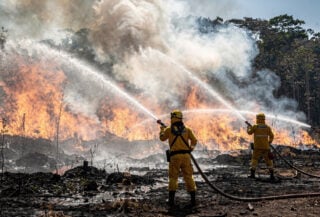 Firefighters spraying water at burning peatland forest in Kalimantan, thick smoke and flames visible