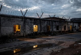 Guarded compound with barbed wire walls, Myanmar-Thailand border region, dusk lighting