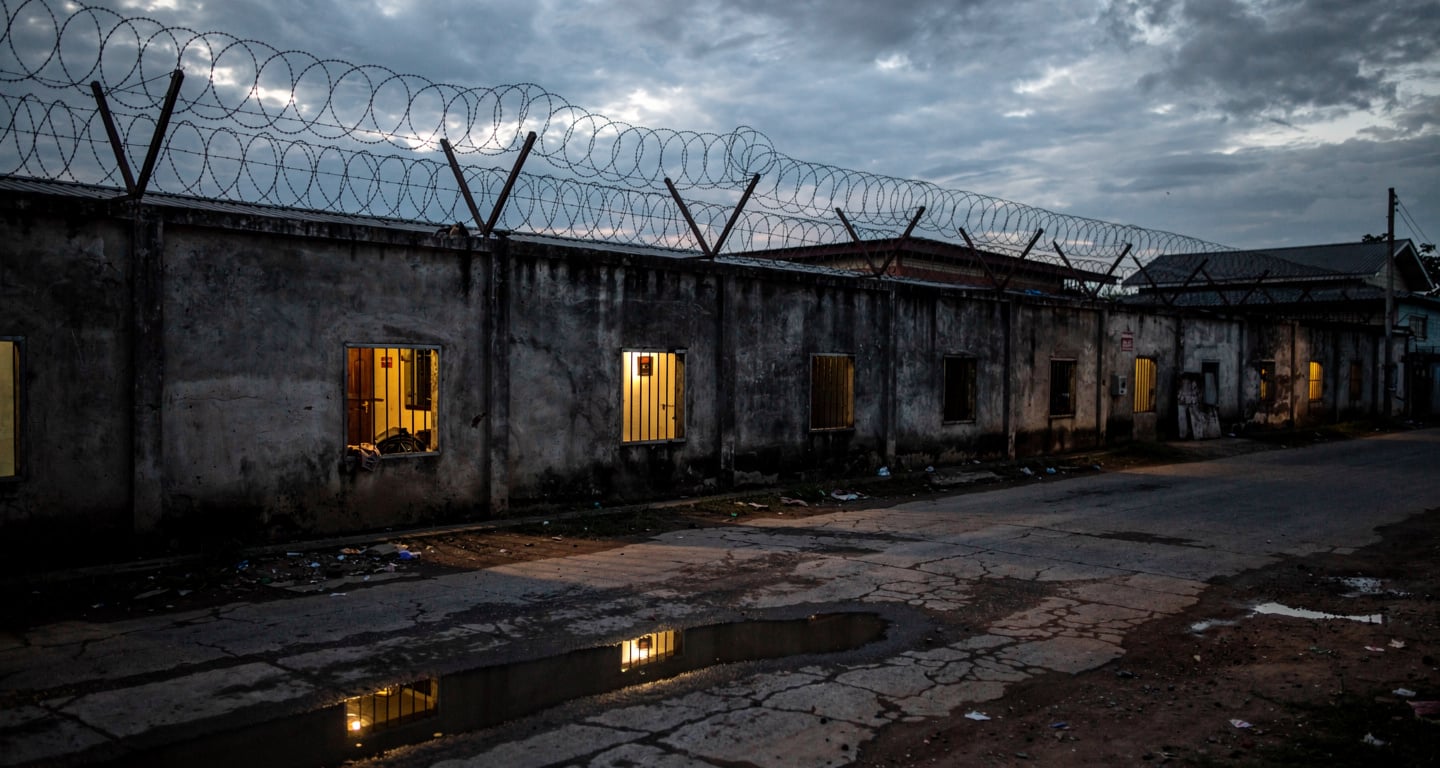 Guarded compound with barbed wire walls, Myanmar-Thailand border region, dusk lighting