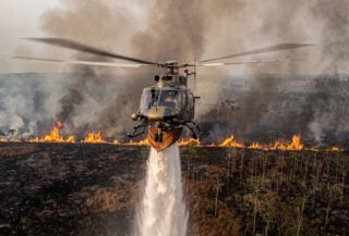 Helicopter conducting water-bombing run over burning peatland in Kalimantan, smoke and flames visible below