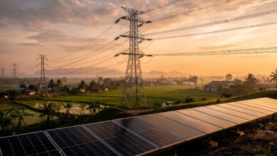 High-voltage transmission towers and power lines crossing Southeast Asian landscape with solar panels below, dusk lighting