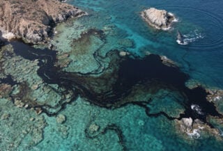 Oil slick spreading across Arabian Sea near Hallaniyat Islands, Oman, with whale visible at edge of contaminated waters