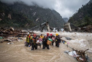 Rescue workers moving through debris-laden floodwaters in Nepal Himalayan valley after glacier collapse