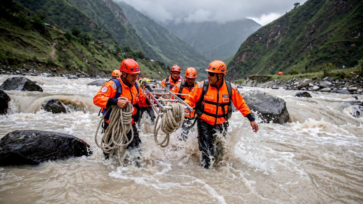 Rescue workers hauling equipment through flooded Himalayan river valley in Rasuwa district, Nepal