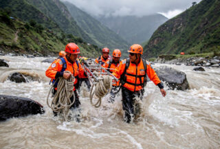 Rescue workers hauling equipment through flooded Himalayan river valley in Rasuwa district, Nepal