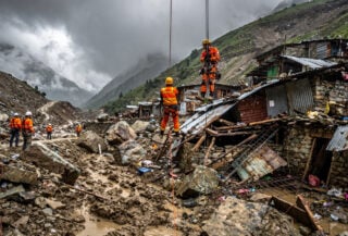Rescue workers rappelling down debris-scarred Himalayan valley searching destroyed homes after glacier flood