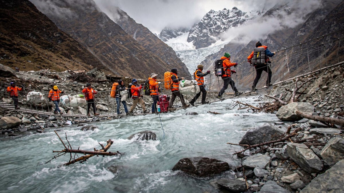 Rescue workers crossing rope bridge over swollen glacial river in Nepal Himalayan valley after glacier collapse