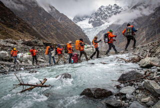 Rescue workers crossing rope bridge over swollen glacial river in Nepal Himalayan valley after glacier collapse