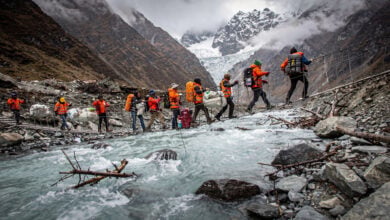 Rescue workers crossing rope bridge over swollen glacial river in Nepal Himalayan valley after glacier collapse