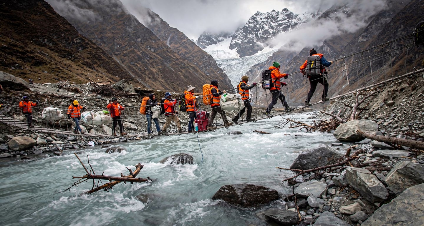 Rescue workers crossing rope bridge over swollen glacial river in Nepal Himalayan valley after glacier collapse