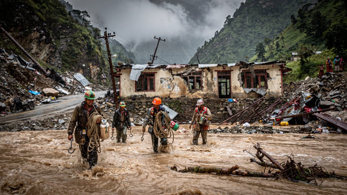 Rescue workers wading through floodwater in Himalayan valley with destroyed customs buildings, Rasuwa district