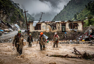 Rescue workers wading through floodwater in Himalayan valley with destroyed customs buildings, Rasuwa district