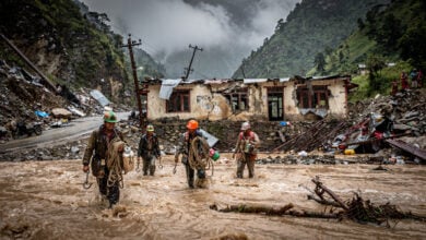 Rescue workers wading through floodwater in Himalayan valley with destroyed customs buildings, Rasuwa district