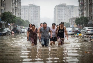 Residents wading through floodwater on Beijing street during heavy rainfall, apartment buildings in background