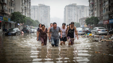 Residents wading through floodwater on Beijing street during heavy rainfall, apartment buildings in background
