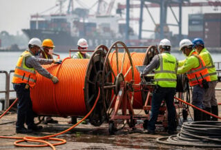 Technicians installing submarine fiber cable at Jakarta port, orange spools and industrial equipment visible