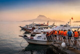 Tourist boats loading passengers at Marina Labuan Bajo, Komodo island in background, dawn light