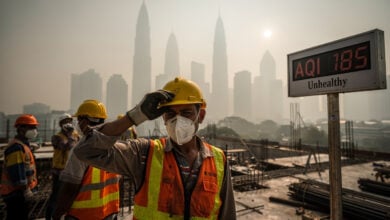 Construction workers in masks on hazy Kuala Lumpur site, one wiping sweat, midday light