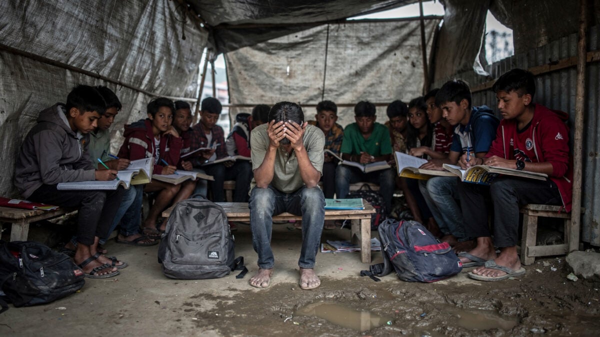 Displaced Nepali students in temporary shelter after glacier flood, Kathmandu, heads down over notebooks