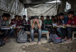 Displaced Nepali students in temporary shelter after glacier flood, Kathmandu, heads down over notebooks