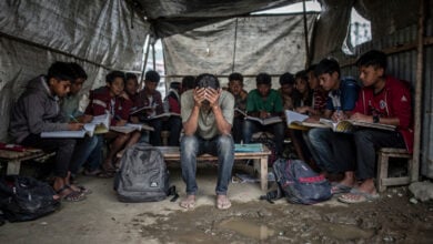 Displaced Nepali students in temporary shelter after glacier flood, Kathmandu, heads down over notebooks