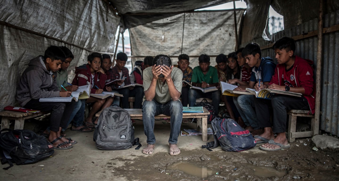 Displaced Nepali students in temporary shelter after glacier flood, Kathmandu, heads down over notebooks