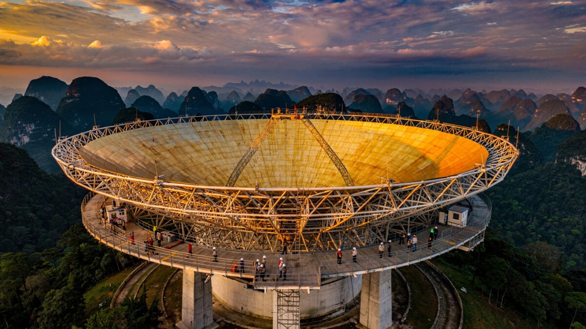 FAST radio telescope dish in Guizhou at dusk with observation platform, golden light on massive spherical surface