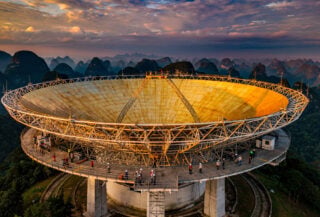 FAST radio telescope dish in Guizhou at dusk with observation platform, golden light on massive spherical surface