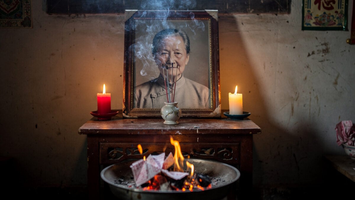 Framed photograph on altar with incense smoke and burning paper offerings, Zhejiang home