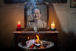 Framed photograph on altar with incense smoke and burning paper offerings, Zhejiang home