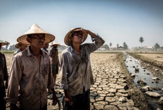 Indonesian farmers in dried rice paddy with empty irrigation canal, drought conditions, harsh sunlight
