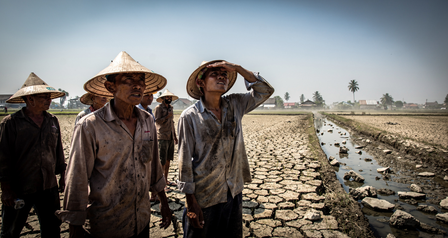 Indonesian farmers in dried rice paddy with empty irrigation canal, drought conditions, harsh sunlight