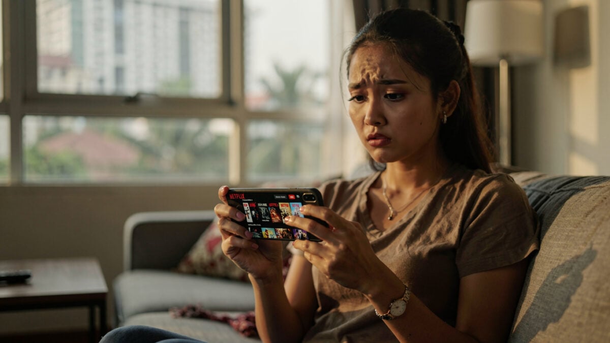 Indonesian woman scrolling Netflix on smartphone, Jakarta apartment, afternoon light