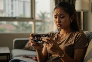 Indonesian woman scrolling Netflix on smartphone, Jakarta apartment, afternoon light