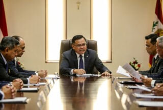 Malaysian cabinet officials at formal government table, one minister visibly tense, Kuala Lumpur