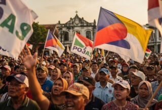 Malaysian political rally supporters holding party flags at Melaka campaign event, afternoon light