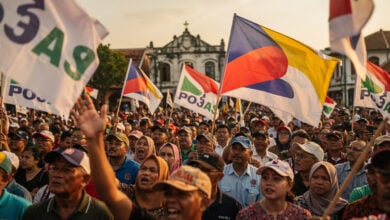 Malaysian political rally supporters holding party flags at Melaka campaign event, afternoon light