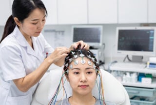 Medical technician placing EEG electrodes on patient scalp in Beijing hospital neurology lab