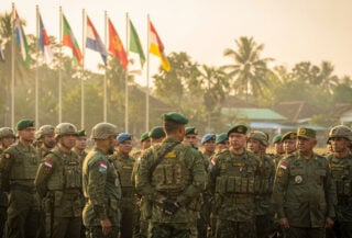 Military personnel from multiple nations in formation at Bandung briefing, participating country flags visible