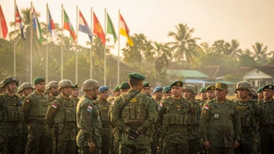 Military personnel from multiple nations in formation at Bandung briefing, participating country flags visible