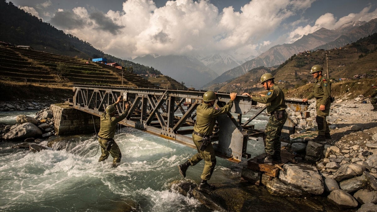 Nepali Army engineers assembling Bailey bridge across flooded mountain river, Nuwakot district, afternoon light