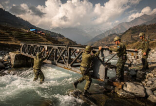 Nepali Army engineers assembling Bailey bridge across flooded mountain river, Nuwakot district, afternoon light