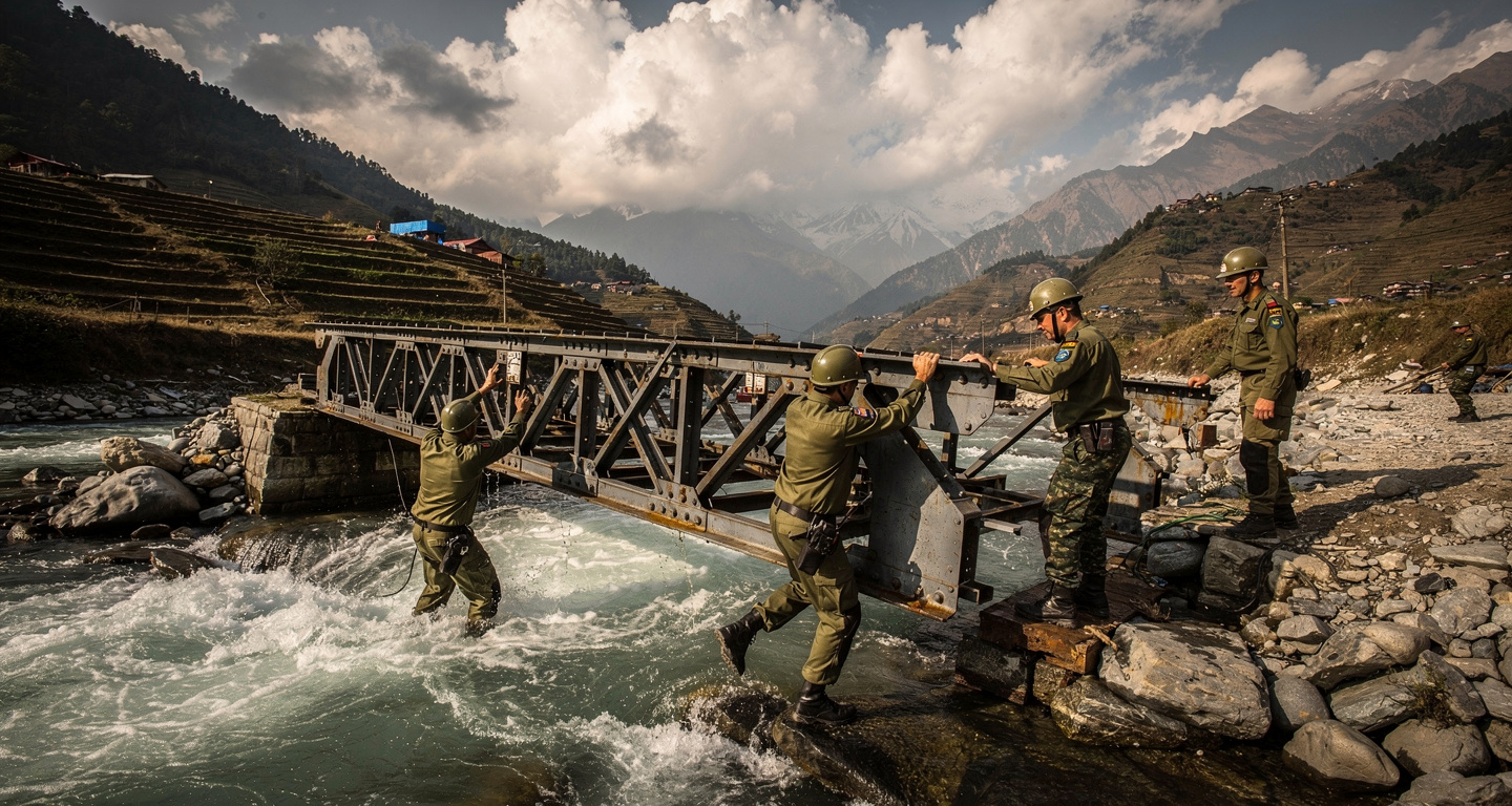 Nepali Army engineers assembling Bailey bridge across flooded mountain river, Nuwakot district, afternoon light