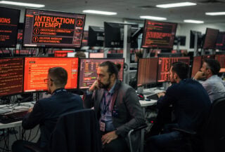 Network operations staff monitoring intrusion alerts on red screens in Australian government facility