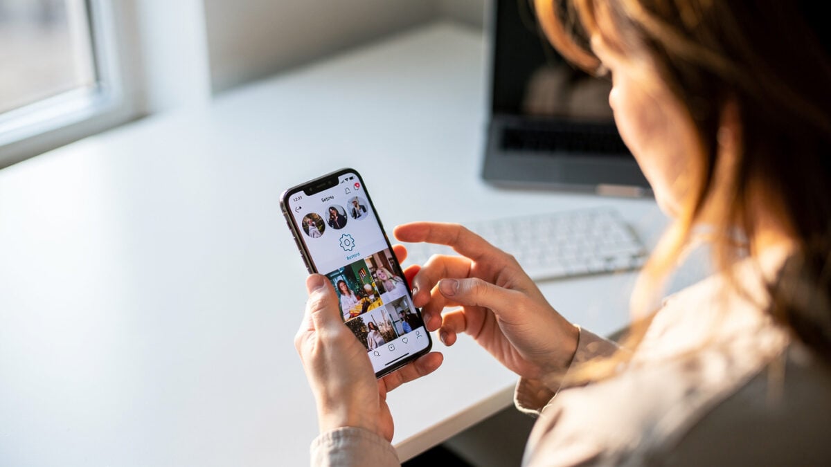 Person scrolling smartphone feed with hand near settings icon, office daylight
