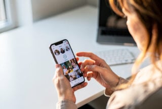 Person scrolling smartphone feed with hand near settings icon, office daylight