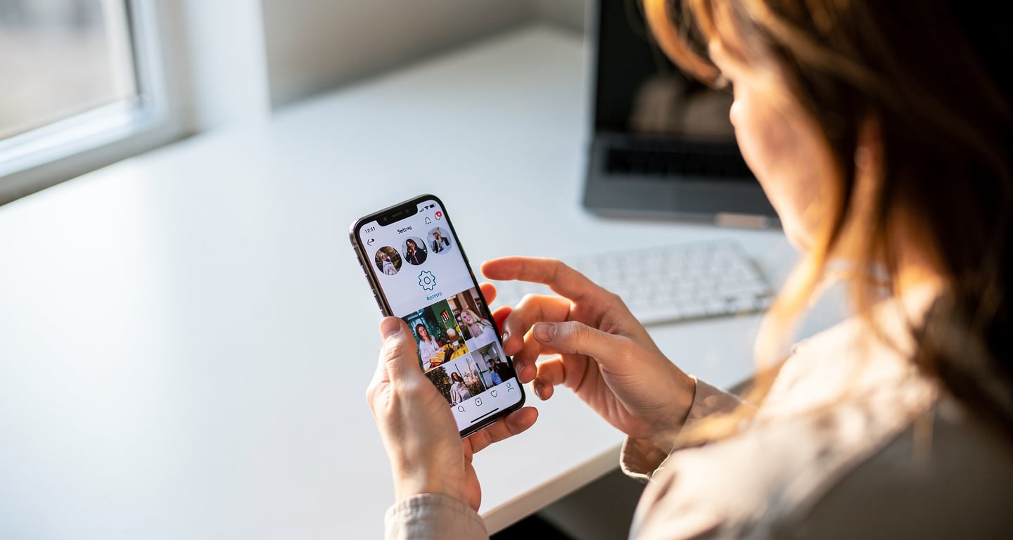 Person scrolling smartphone feed with hand near settings icon, office daylight