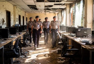 Police officers inspecting abandoned scam compound in Phnom Penh, empty desks and computers visible
